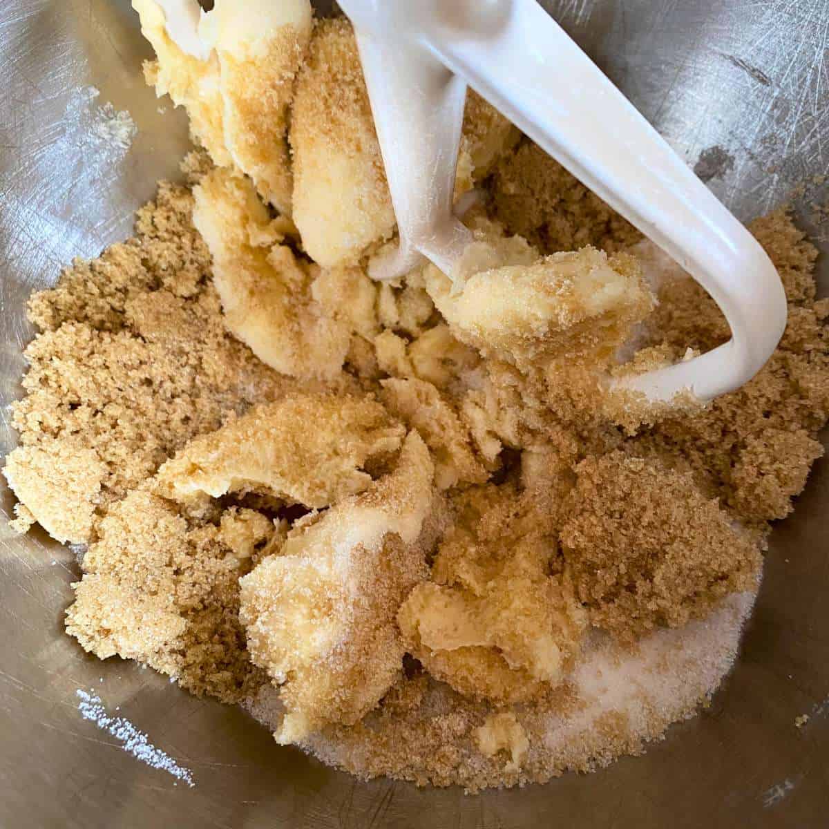 A stand mixer paddle mixing together dairy free margarine, granulated sugar, and brown sugar.