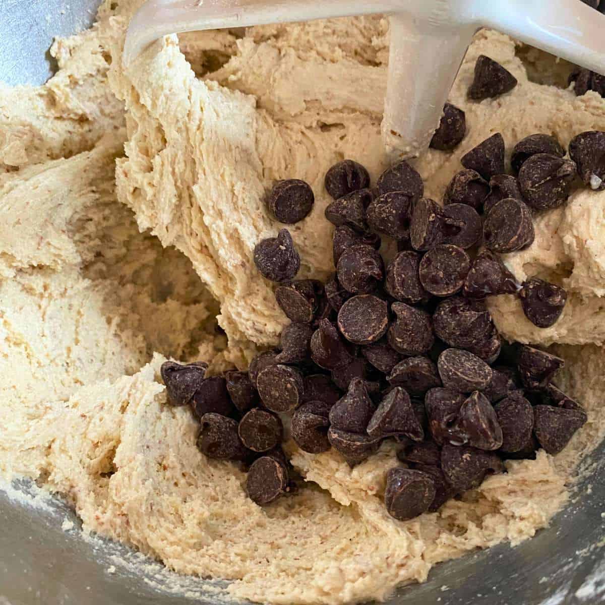 Cookie dough with chocolate chips being added to the mixing bowl.