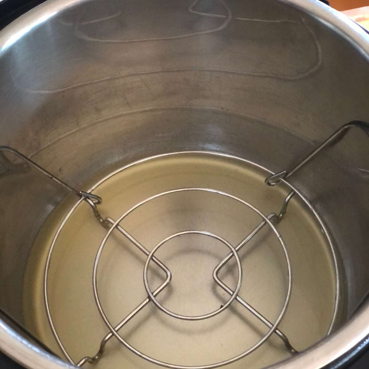 A pressure cooker pot with chicken broth and the trivet inside.