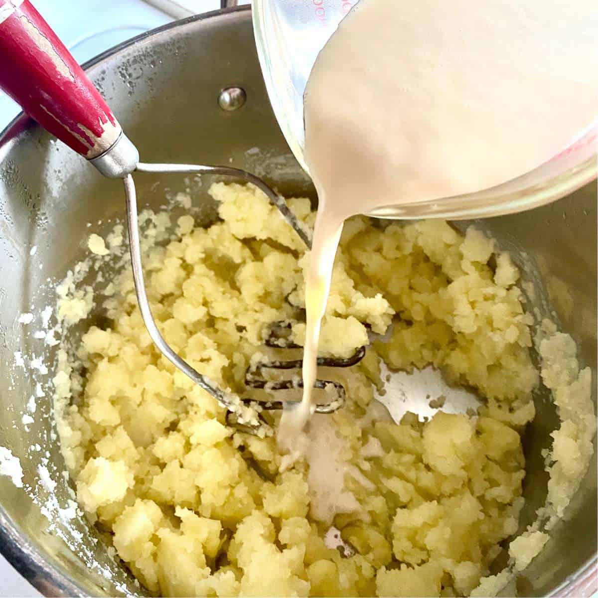 Dairy free milk being added to partially mashed potatoes.