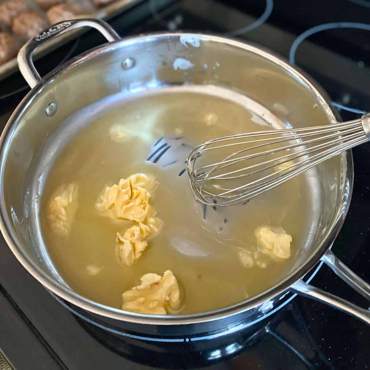 Dairy free margarine being melted in a large skillet while being stirred with a whisk.