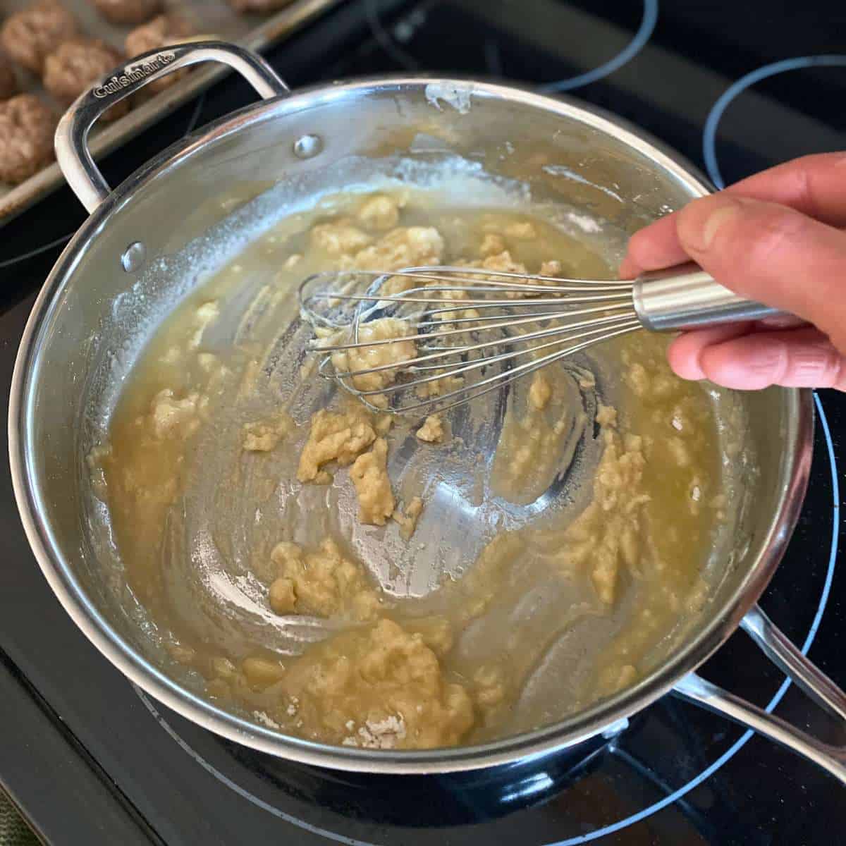 Gluten free flour being stirred into the dairy free margarine with a whisk in a large skillet.