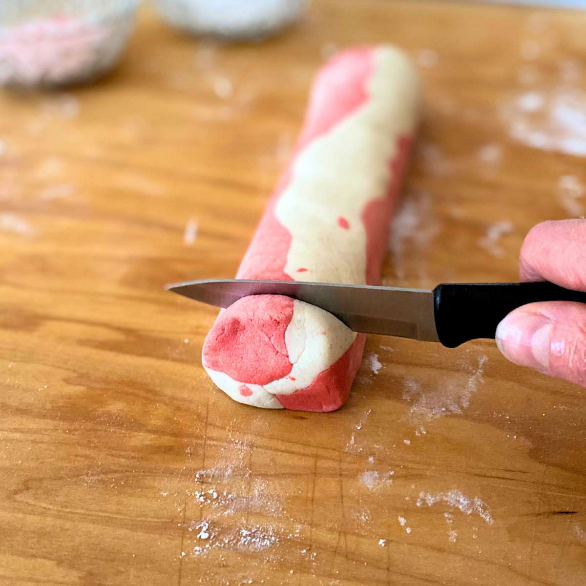 A paring knife cutting through the log of cookie dough.