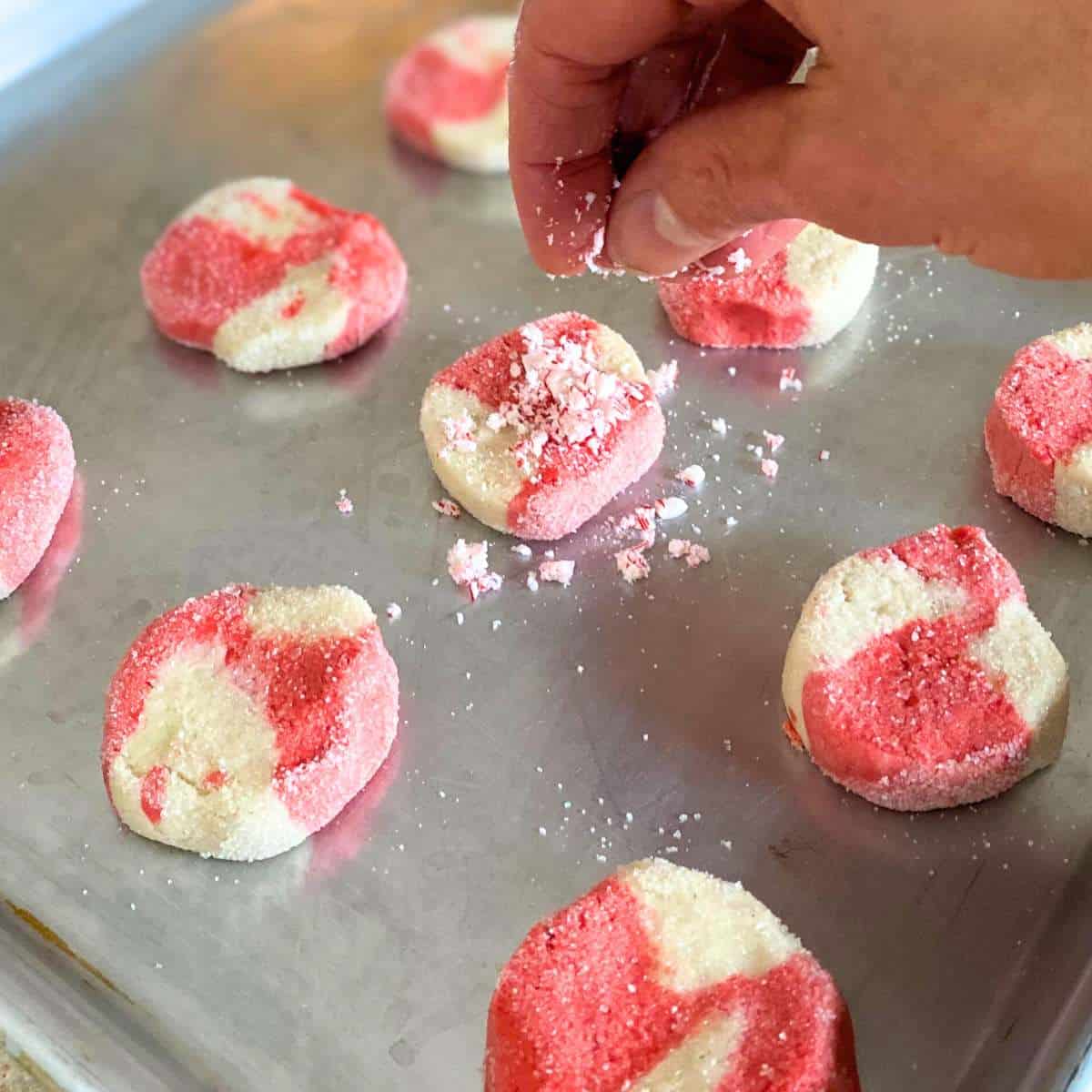 A candy cane cookie being sprinkled with candy cane pieces.