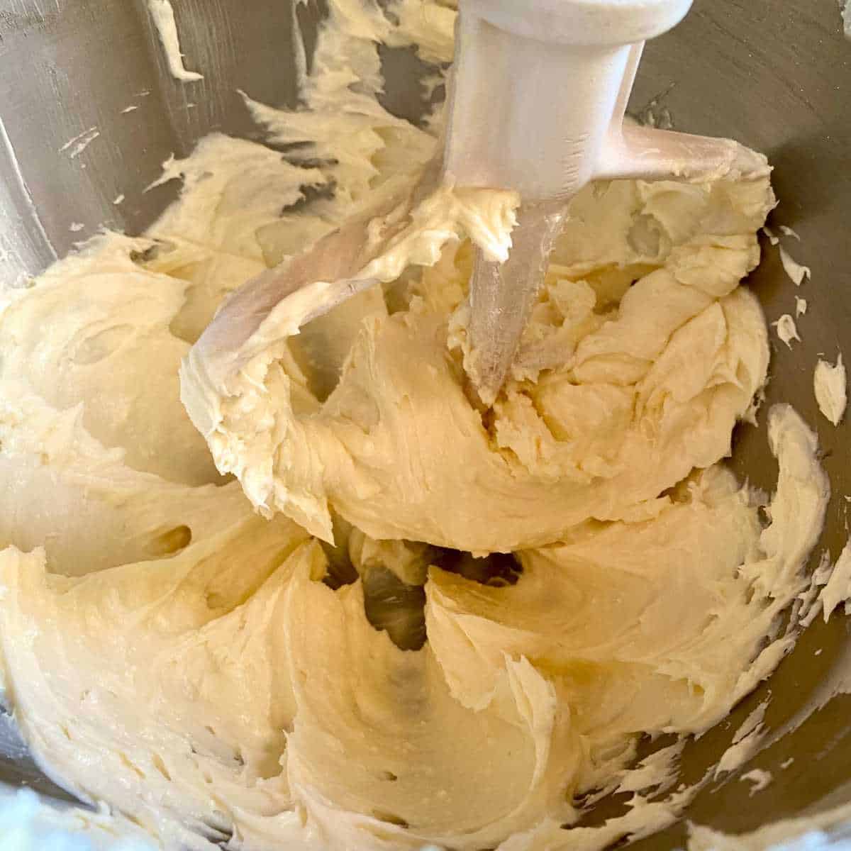 Dairy free margarine and powdered sugar being mixed with a mixer paddle.