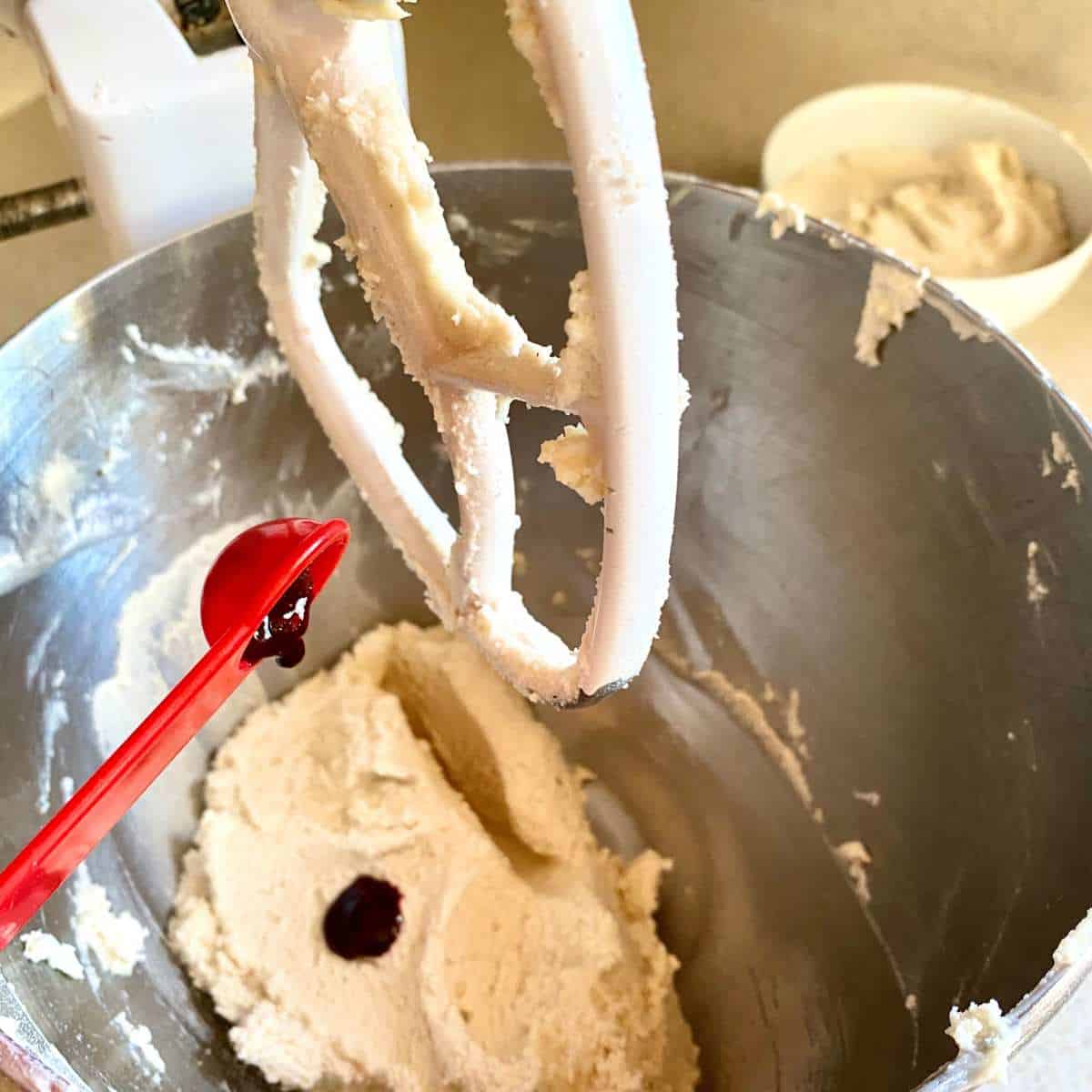 Red food coloring being added to half of the cookie dough in a mixing bowl.