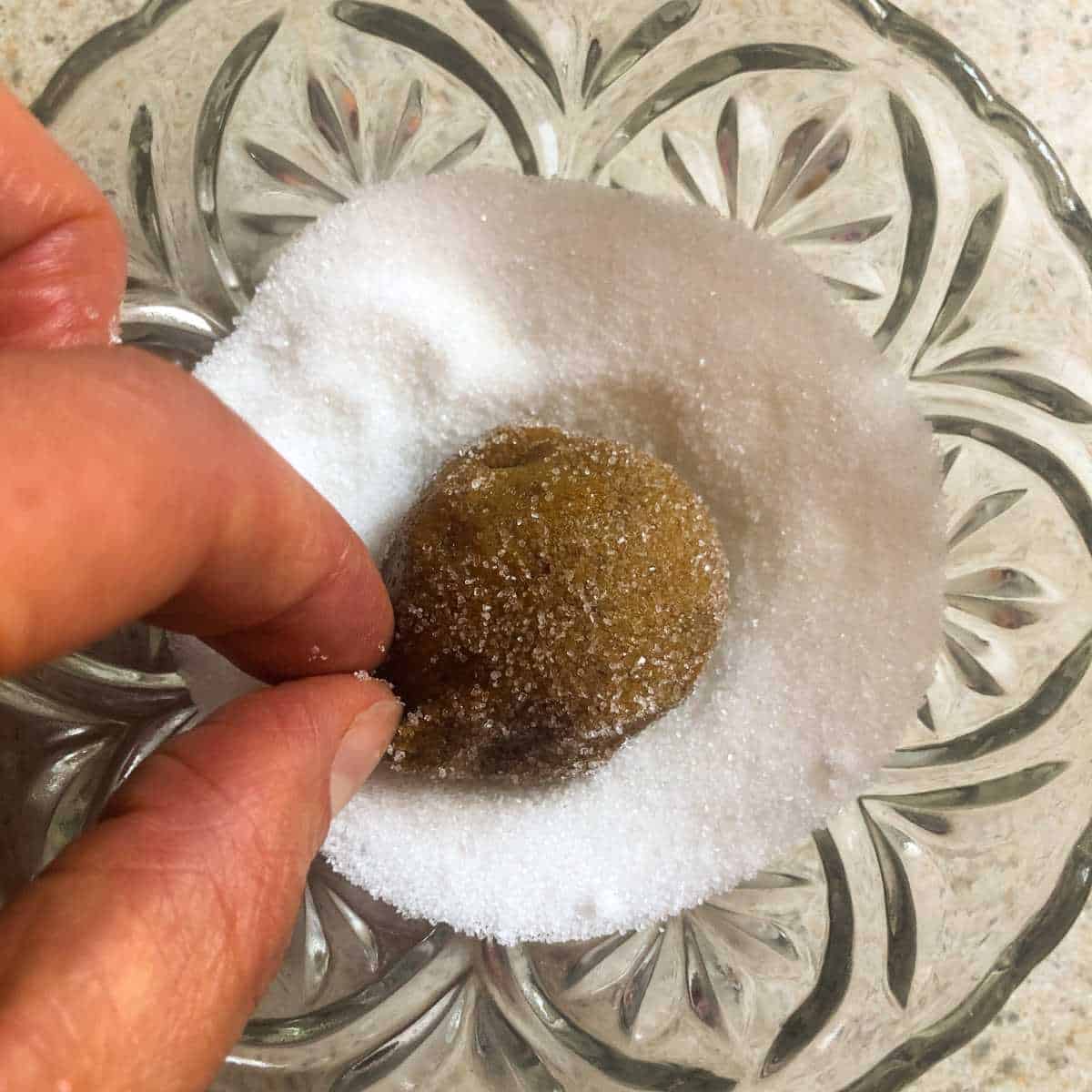 Rolling gluten free ginger cookie dough in a bowl of sugar.
