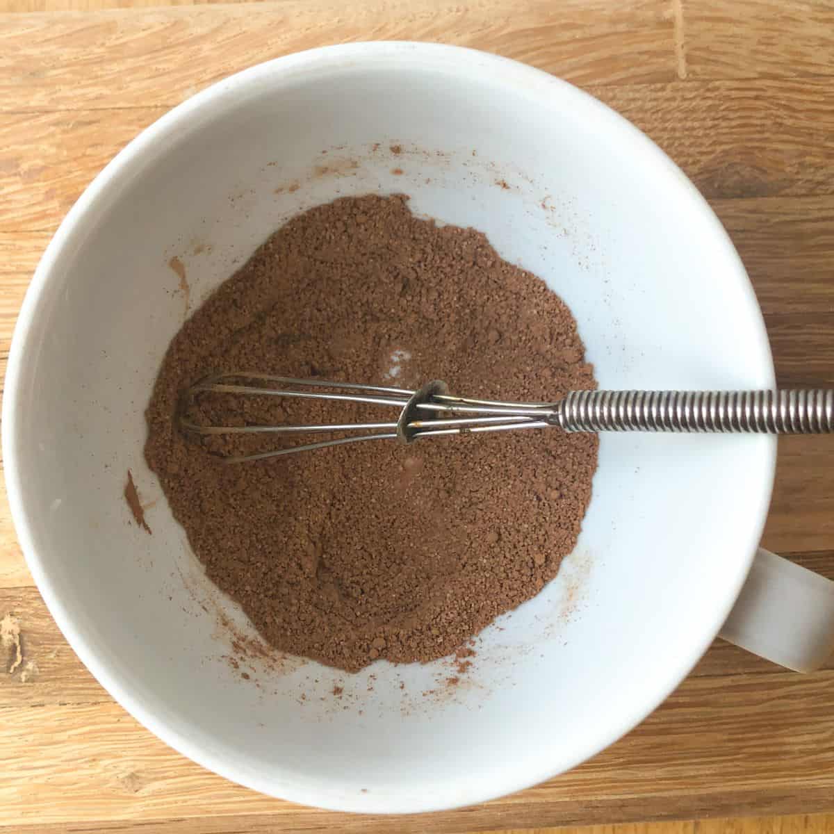 Cocoa powder, sugar, and salt being mixed with a whisk in a mug.