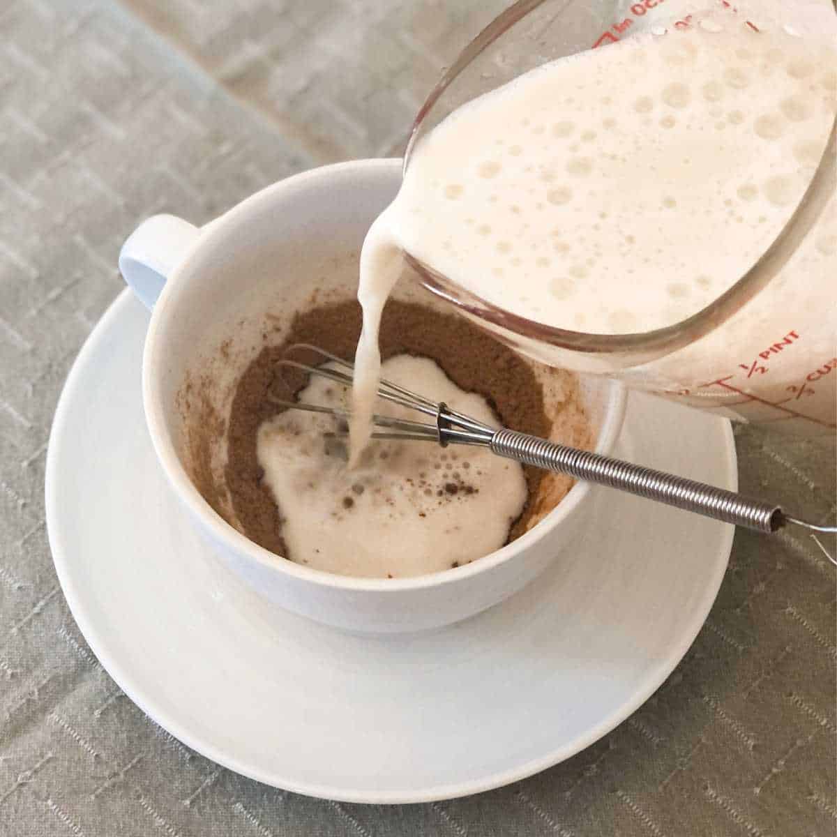 Hot oat milk being poured into a mug with cocoa powder, sugar, and salt.